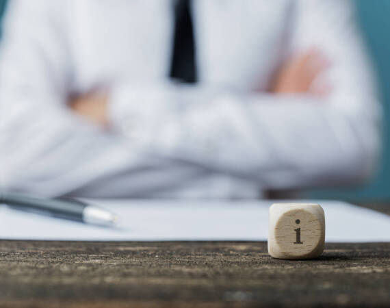 Businessman sitting at his desk with pen and paper in front of him and a dice wit letter i on it. Conceptual image of service and information.